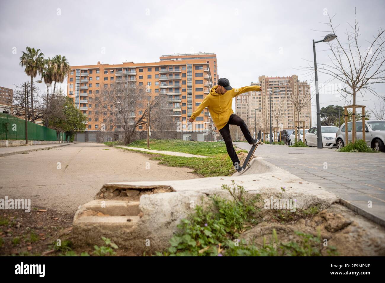 Hombre joven de Italia en una sudadera con capucha amarilla y negra gorra saltando con su skate Foto de stock