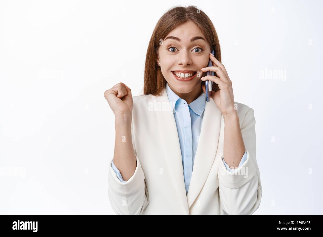 Feliz mujer de oficina, elegante señora en traje blanco responder a la llamada de teléfono y saltar de la felicidad, recibir grandes noticias, ganar y celebrar, de pie encima Foto de stock