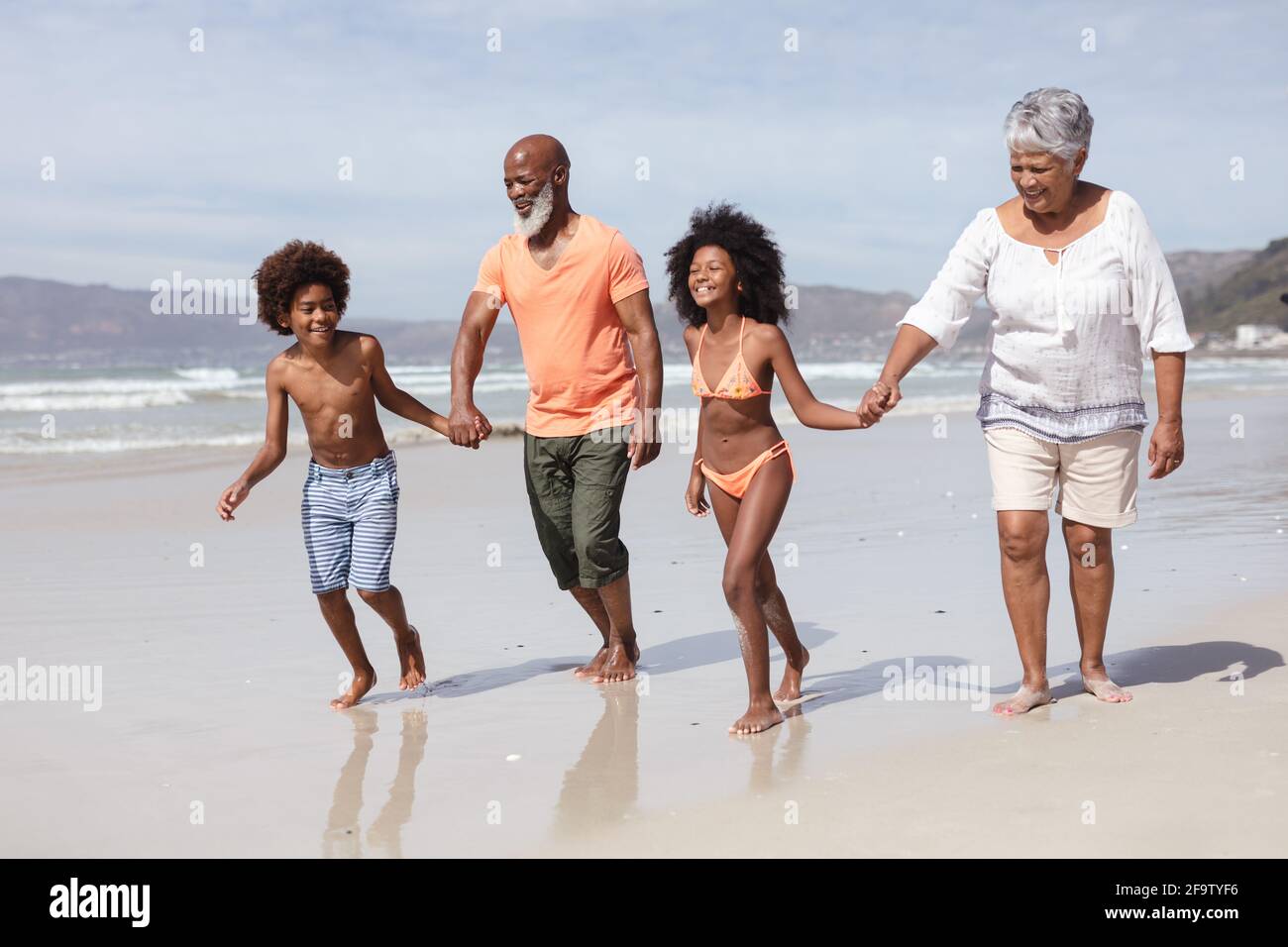 Abuelos y nietos afroamericanos que tienen las manos caminando sobre el playa Foto de stock