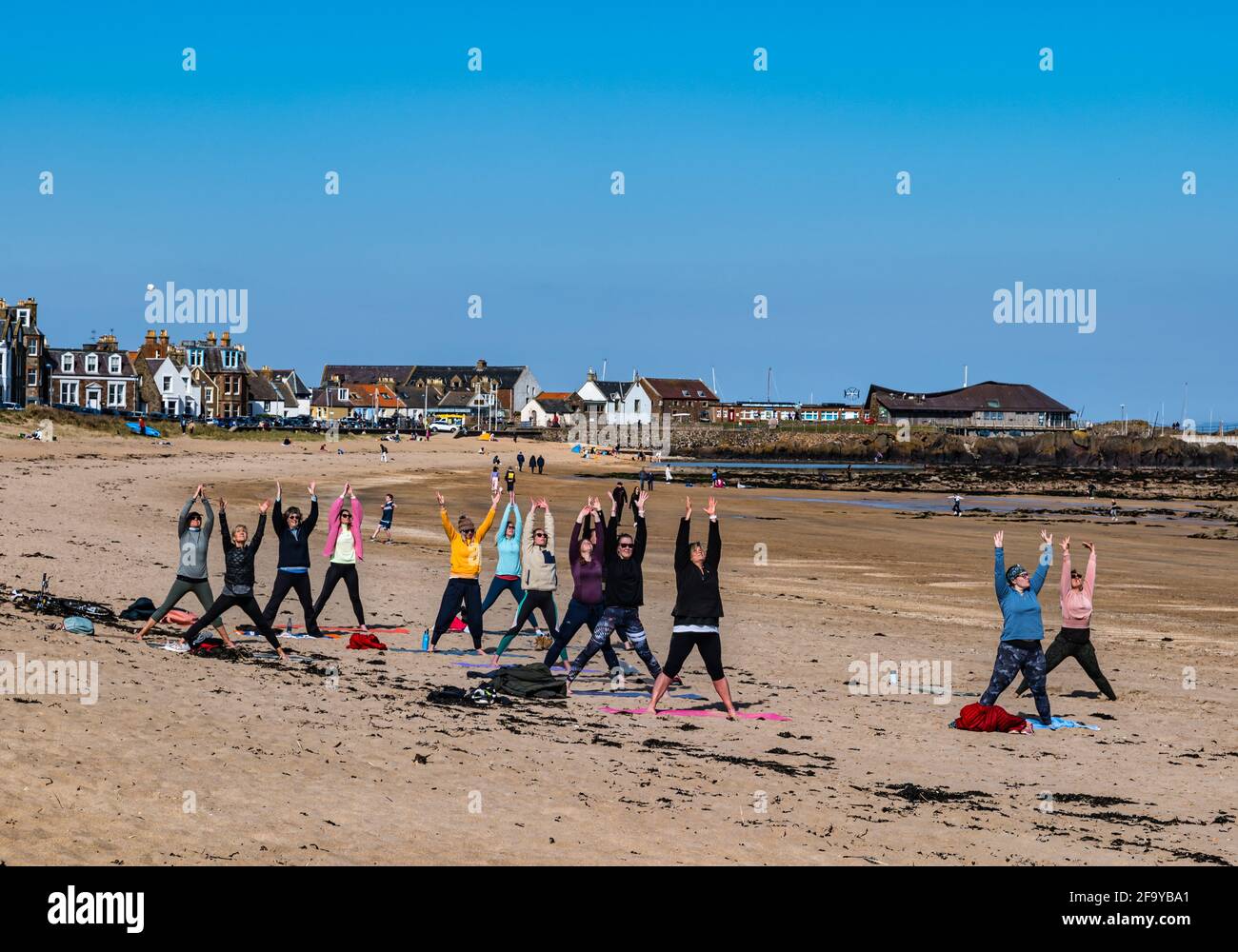 Gente disfrutando de la playa al sol con mujeres en clase de ejercicios de yoga, North Berwick, East Lothian, Escocia, Reino Unido Foto de stock