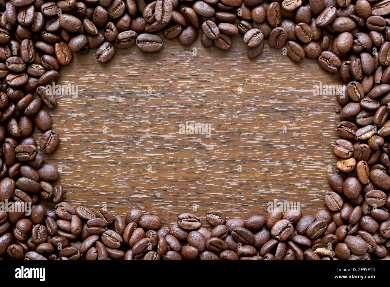 Marco de café. Borde compuesto de granos de café alrededor de un fondo de efecto de madera Foto de stock