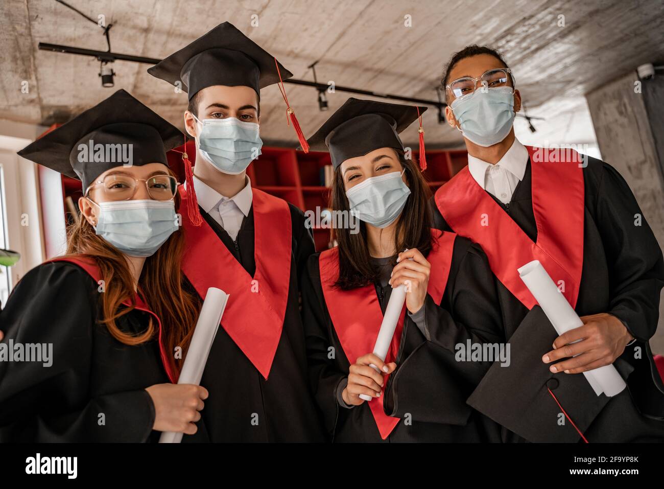 estudiantes multiétnicos en máscaras médicas, batas de graduación y caps con diploma, de 2021 años de edad Foto de stock