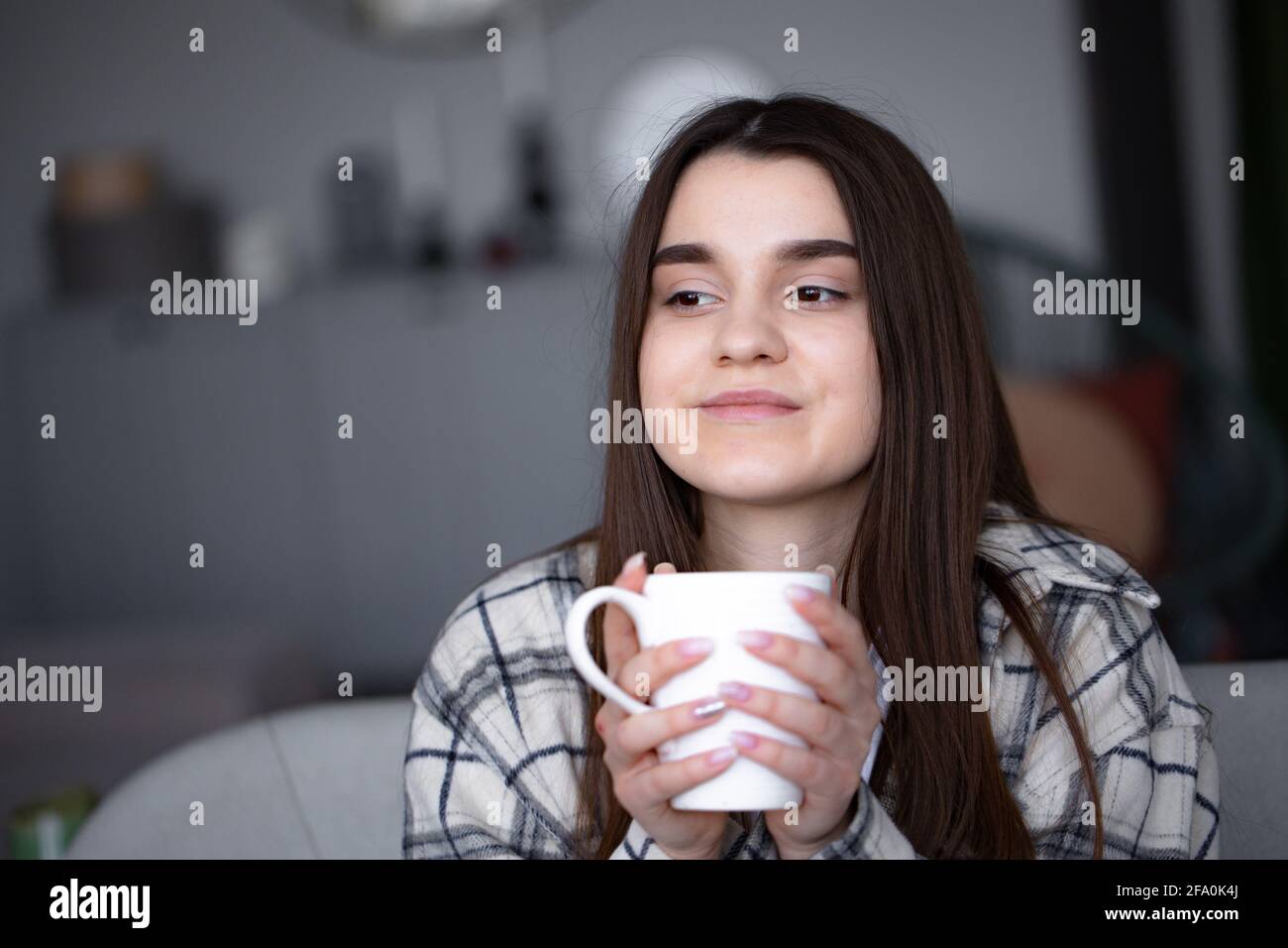 Mujeres sentadas en un sofá acogedor con manta con café. La mujer se relaja disfrutando de un estilo de vida tranquilo en casa con una taza de té. Espacio de copia. Foto de stock