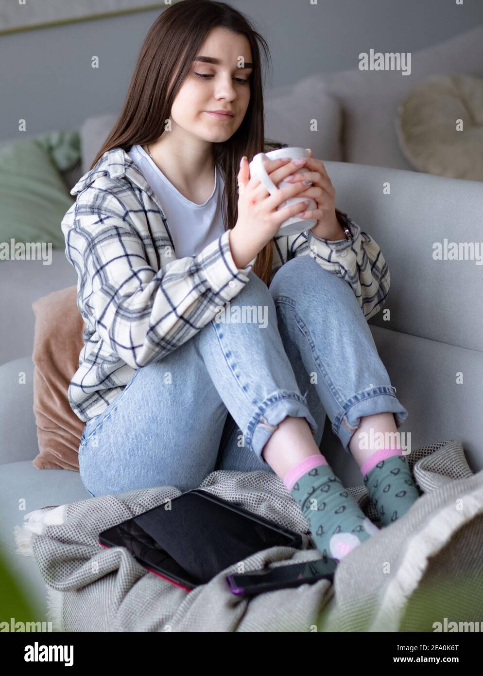 Mujeres sentadas en un sofá acogedor con manta con café. La mujer se relaja disfrutando de un estilo de vida tranquilo en casa con una taza de té. Foto de stock