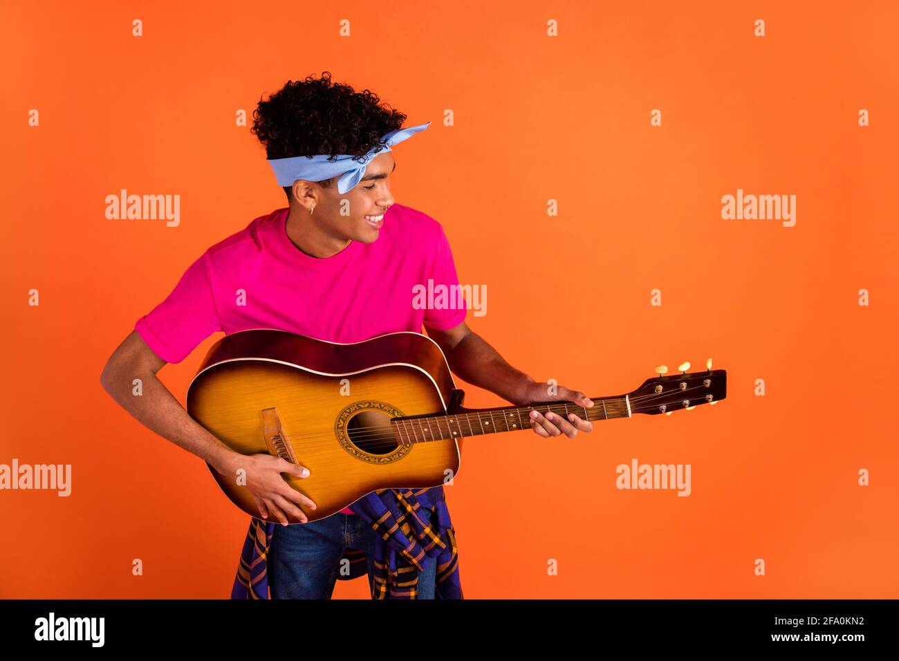 Foto de alegre músico tipo tocar guitarra mirada lateral banda de sujeción  rosa para la camiseta con fondo naranja aislado Fotografía de stock - Alamy