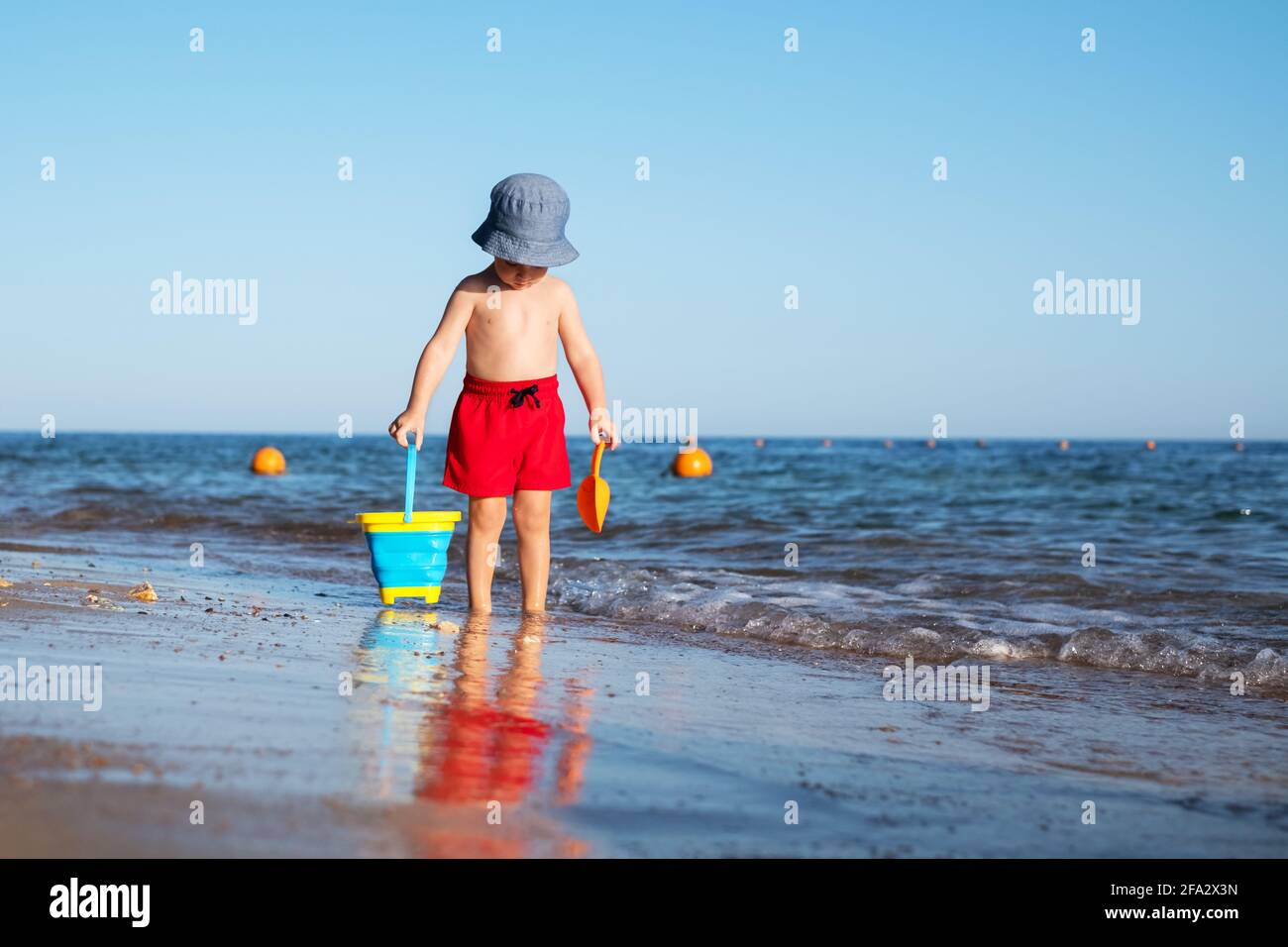 Niño en pantalones cortos rojos en la playa de verano Foto de stock
