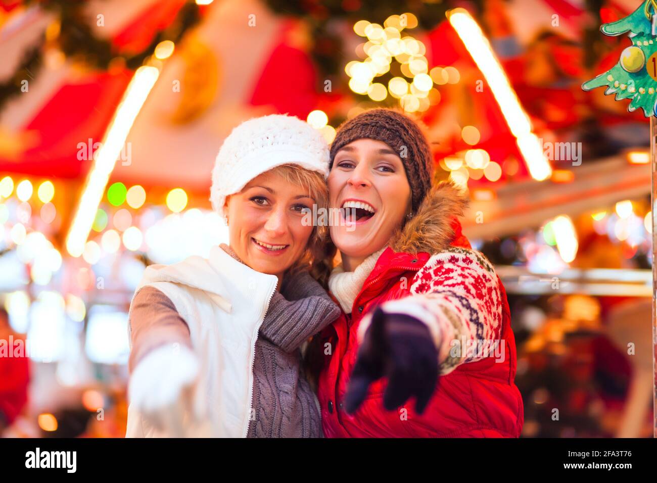 Dos mujeres o amigos durante la temporada de adviento o vacaciones en Frente de un carrusel o de un carrusel en Navidad o Mercado de Navidad Foto de stock