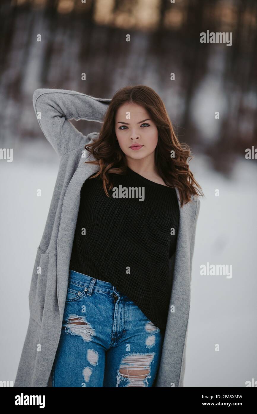 Mujer joven con una camisa negra, jeans y una chaqueta en un parque invierno cubierto de Fotografía de stock -