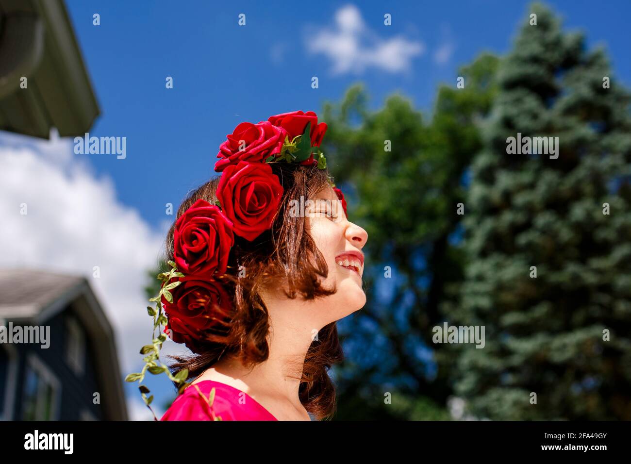 Una chica hermosa con una corona de rosas sonríe debajo un cielo azul Foto de stock
