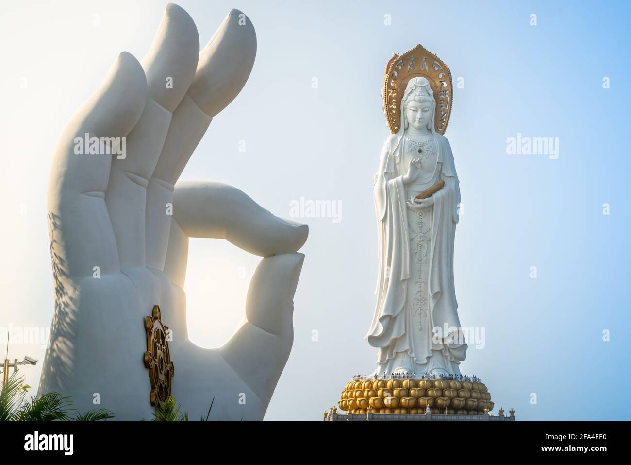 Vista del paisaje de la estatua blanca de la mano con la rueda de Dharma y. Guanyin de la estatua del Mar del Sur en el fondo en Nanshan Budismo parque cultural templo i Foto de stock