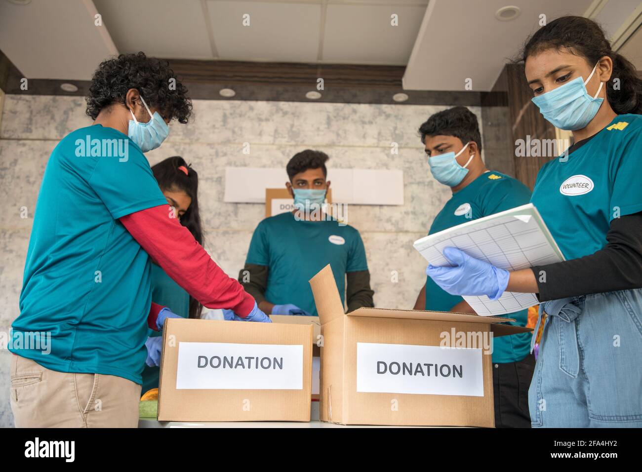Foco en la muchacha delantera, grupo de voluntarios ocupados trabajando arreglando la ropa y las cajas de la donación durante el cierre pandémico del covid-19 del coronavirus - concepto Foto de stock