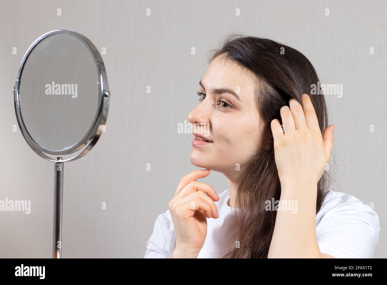 Una mujer morena de 20-30 años mira en el espejo y se admira. Amor propio, cuidado facial de la piel y del cabello, . Piel facial sana para publicidad Foto de stock