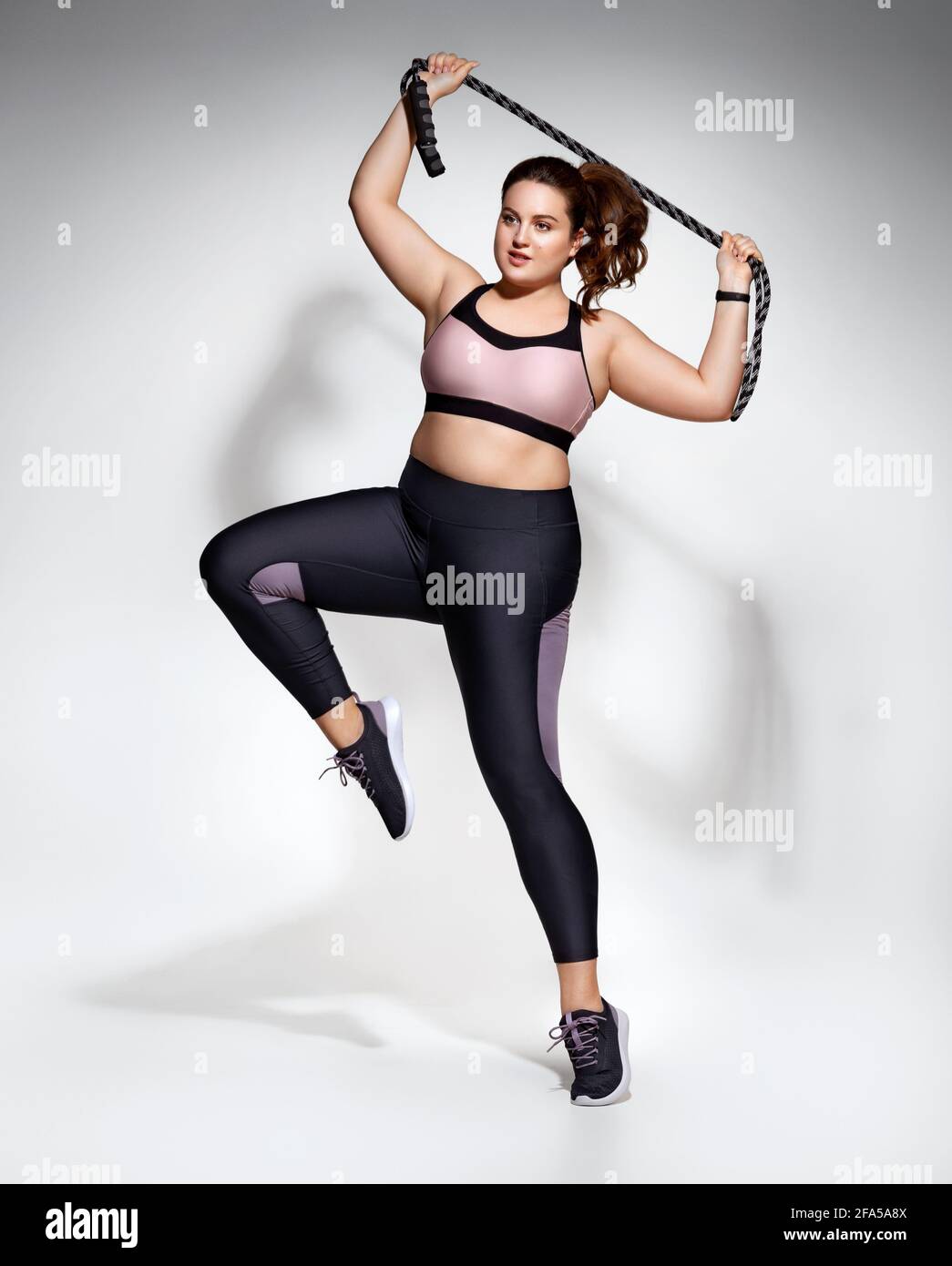 Chica deportiva con cuerda que salta en movimiento. Foto del modelo con figura en ropa deportiva de moda sobre fondo gris. dinámico. Moti deportivo Fotografía de stock - Alamy