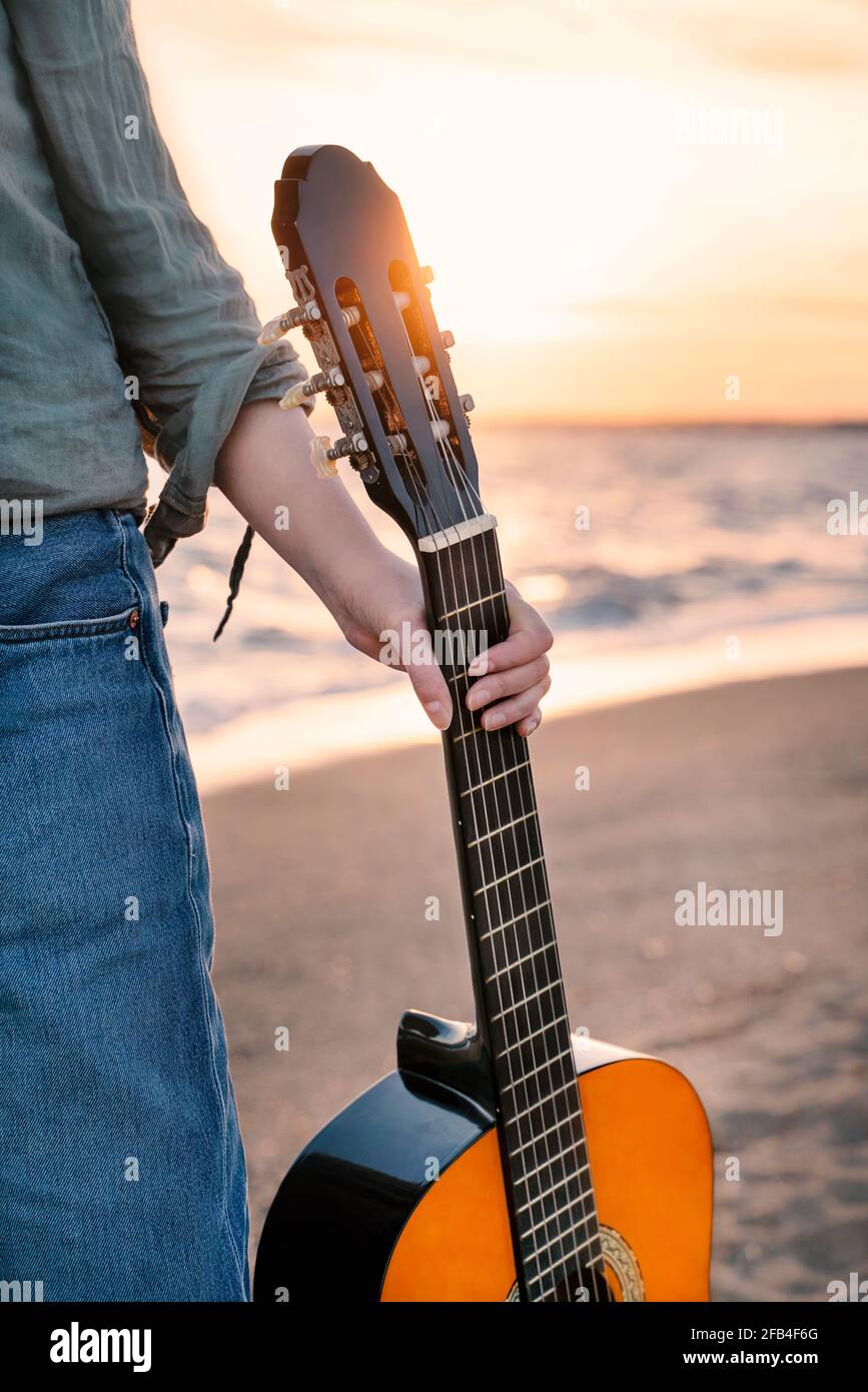 Joven sosteniendo una guitarra clásica en la playa al atardecer Fotografía  de stock - Alamy