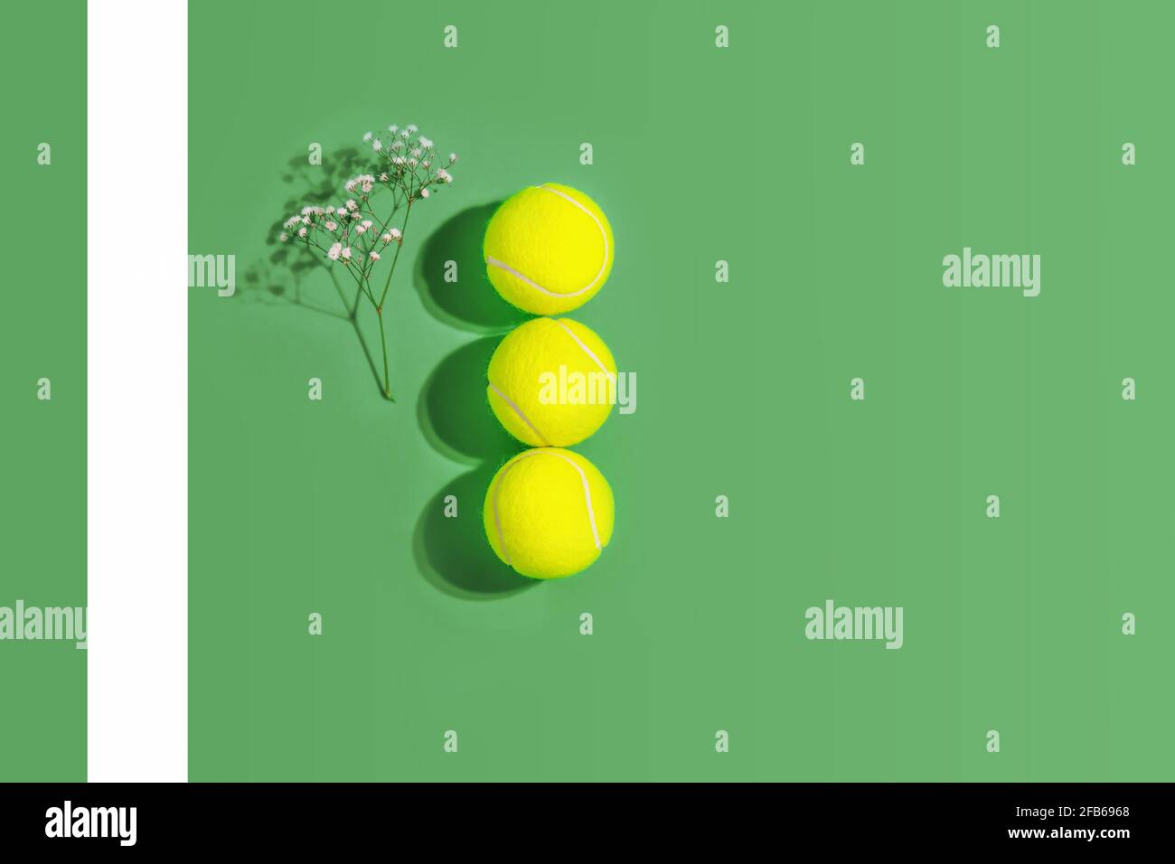 Tenis. Composición deportiva de primavera con tres pelotas de tenis amarillas y flores sobre un fondo verde de pista de tenis dura con espacio para copiar Foto de stock