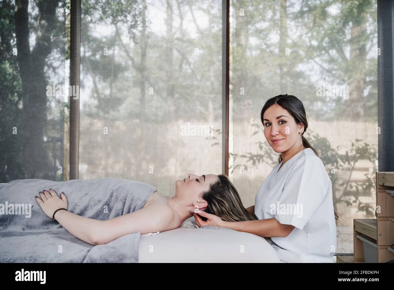 Fisioterapeuta femenina que masajea la cabeza de la paciente acostada sobre la mesa en el hospital Foto de stock