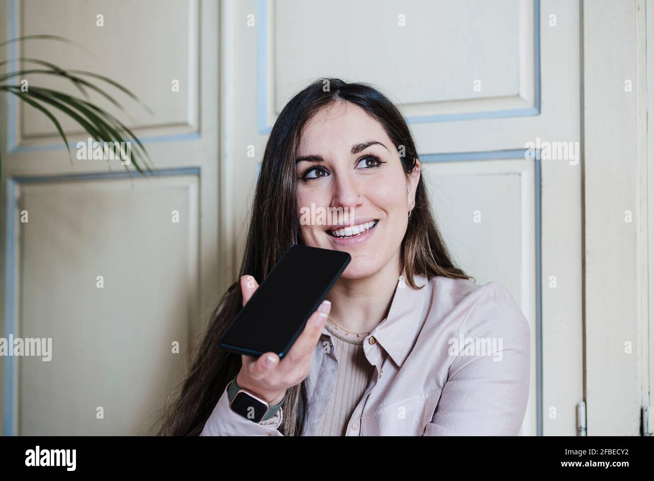 Mujer sonriente utilizando el smartphone para enviar mensajes de voz a. inicio Foto de stock