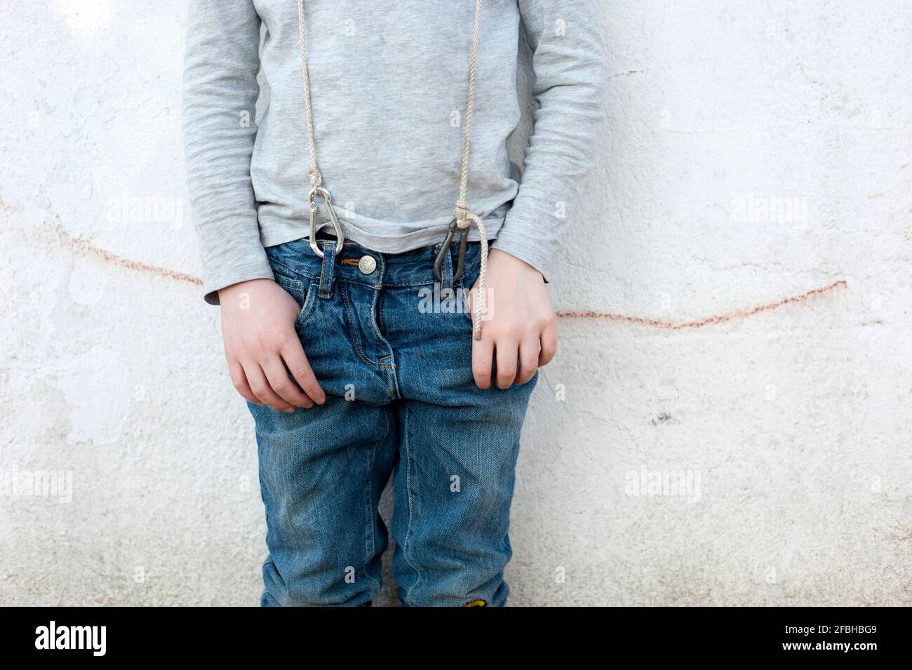 Niño con tirantes de gancho de mosquetón delante de la pared Foto de stock