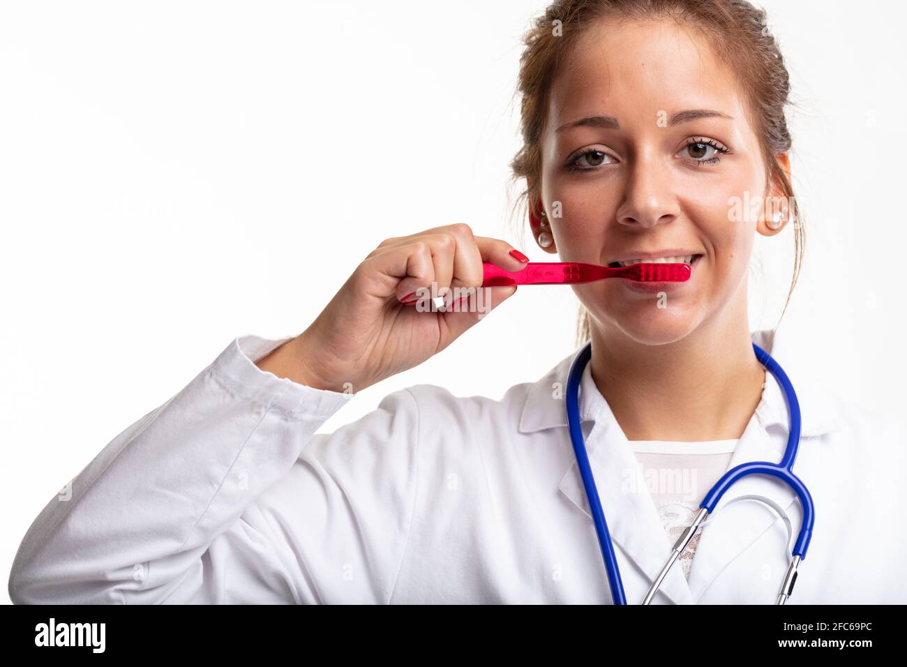 Enfermera dental o dentista que usa bata de laboratorio y estetoscopio demostrando cepillado de los dientes con un cepillo de dientes de plástico rojo en un concepto de higiene dental Foto de stock