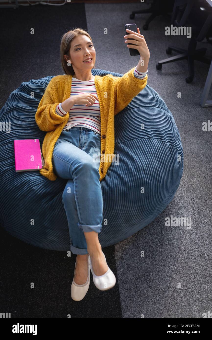 Mujer de negocios mixta de raza que se relaja en la oficina espacio relajante tumbado en bolsa de beanbag Foto de stock