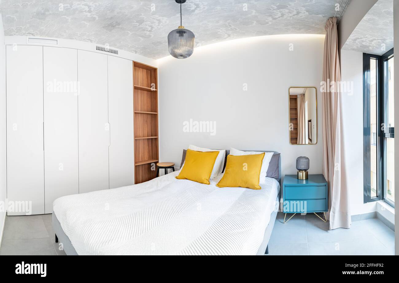 Habitación limpia y luminosa con cama, edredón, mesita de noche, lámparas,  cortina, espejo de metal, luz indirecta LED y papel pintado en el techo.  Diseño minimalista Fotografía de stock - Alamy