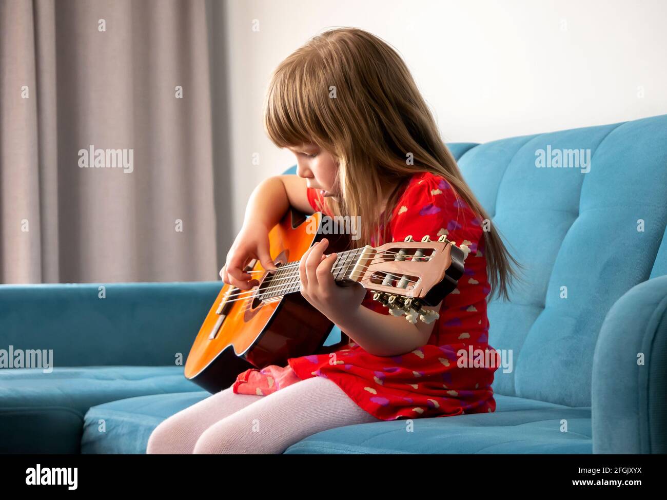 Niña pequeña, joven en edad escolar niño tocando una guitarra acústica,  practicando un instrumento musical sentado en un sofá en casa, interior,  vista lateral. Música Fotografía de stock - Alamy