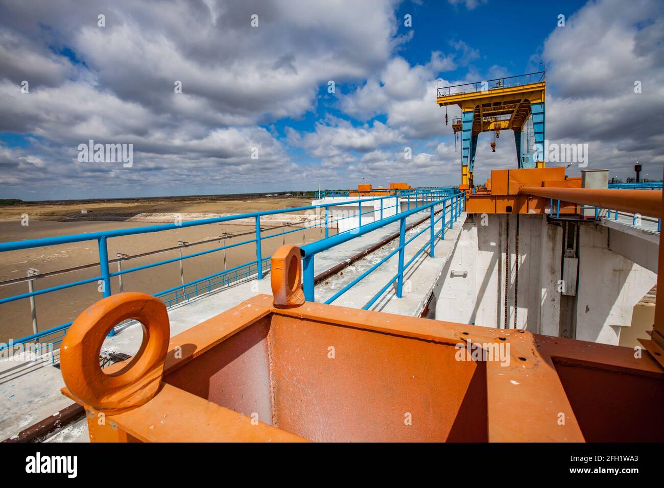 Shardara río dique. Puente de hormigón, grúa de gentry. Cambiador de velocidad naranja en primer plano. Cielo azul con nubes.Ciudad de Kazaly, región de Kyzylorda, Kazajistán. Foto de stock