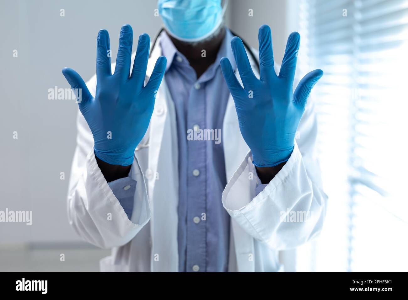 Sección media del médico afroamericano con mascarilla y guantes de látex Foto de stock