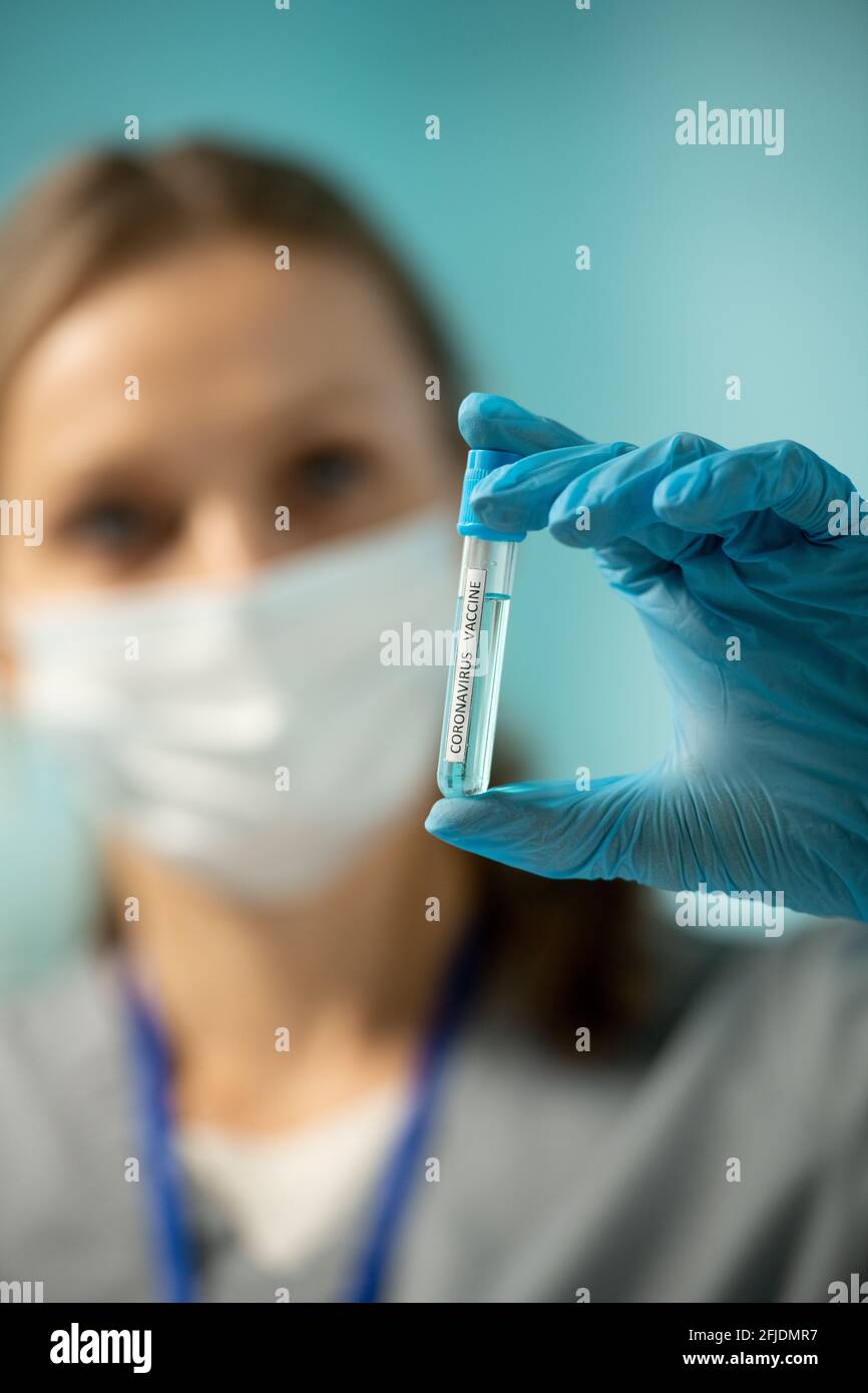 Primer plano de la enfermera femenina en el tubo de ensayo con un guante azul de la vacuna contra el coronavirus mientras se prepara para la vacunación Foto de stock