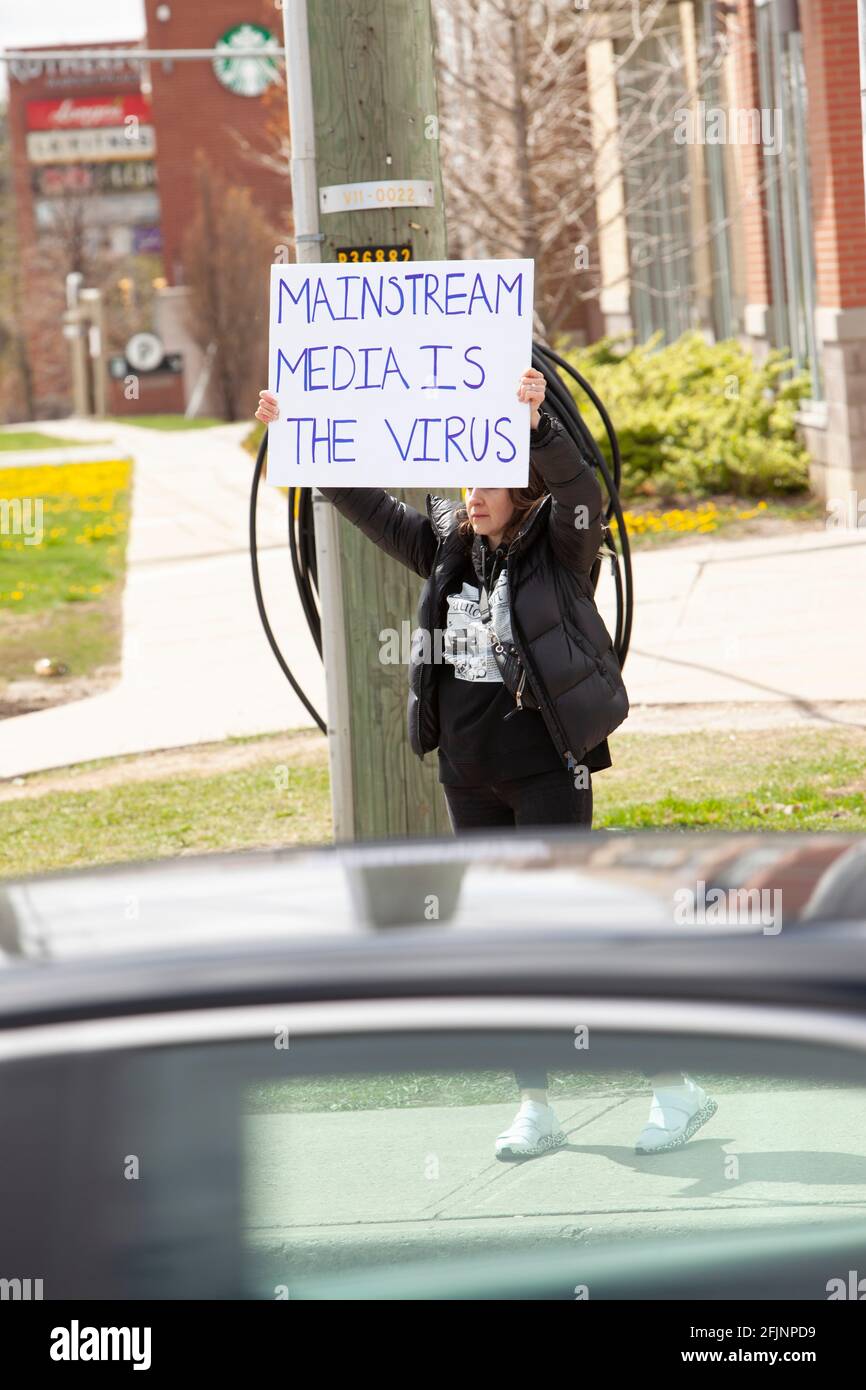 Vaughan, Canadá - 25 de abril de 2021: La mujer que sostiene los medios de comunicación principales es el signo del virus en protesta por las medidas de cierre de COVID-19 en Ontario Foto de stock