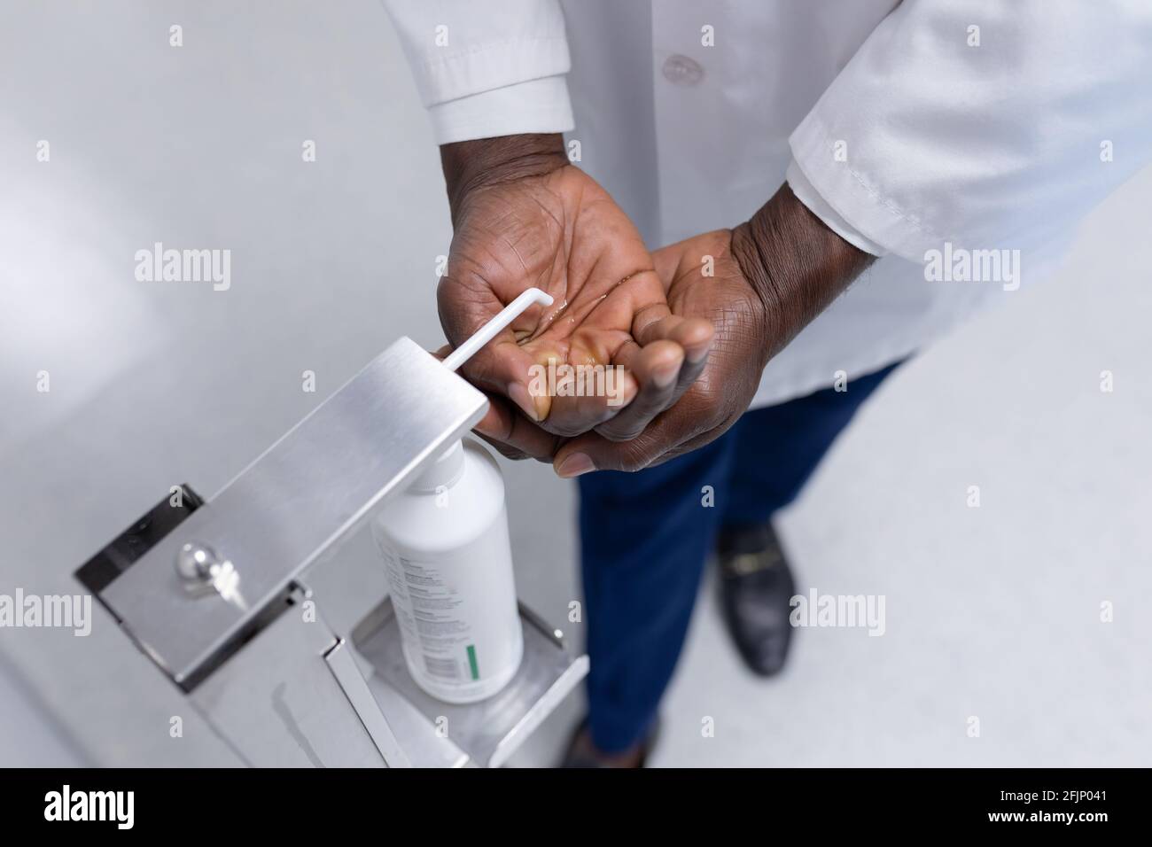 Sección media del médico masculino afroamericano en la desinfección de la capa blanca manos en el pasillo del hospital Foto de stock