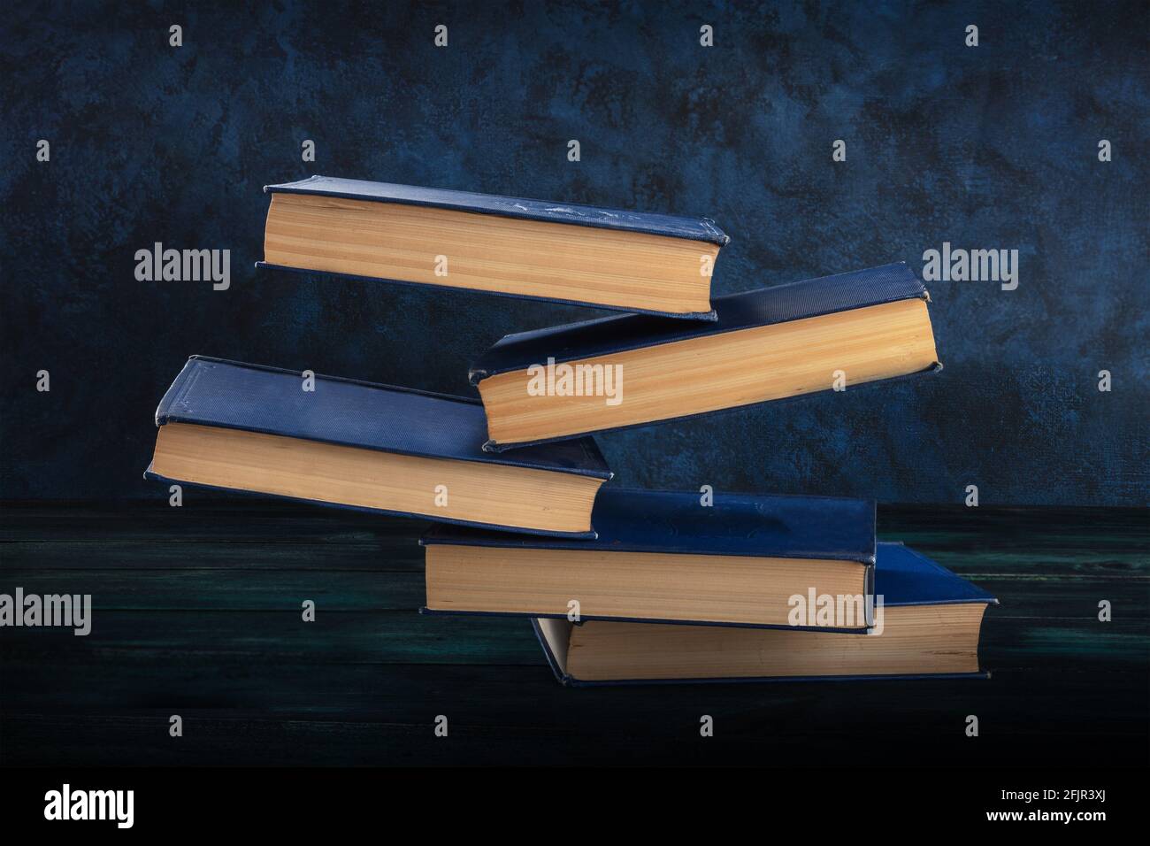Libros cayendo sobre el escritorio sobre un fondo azul Foto de stock