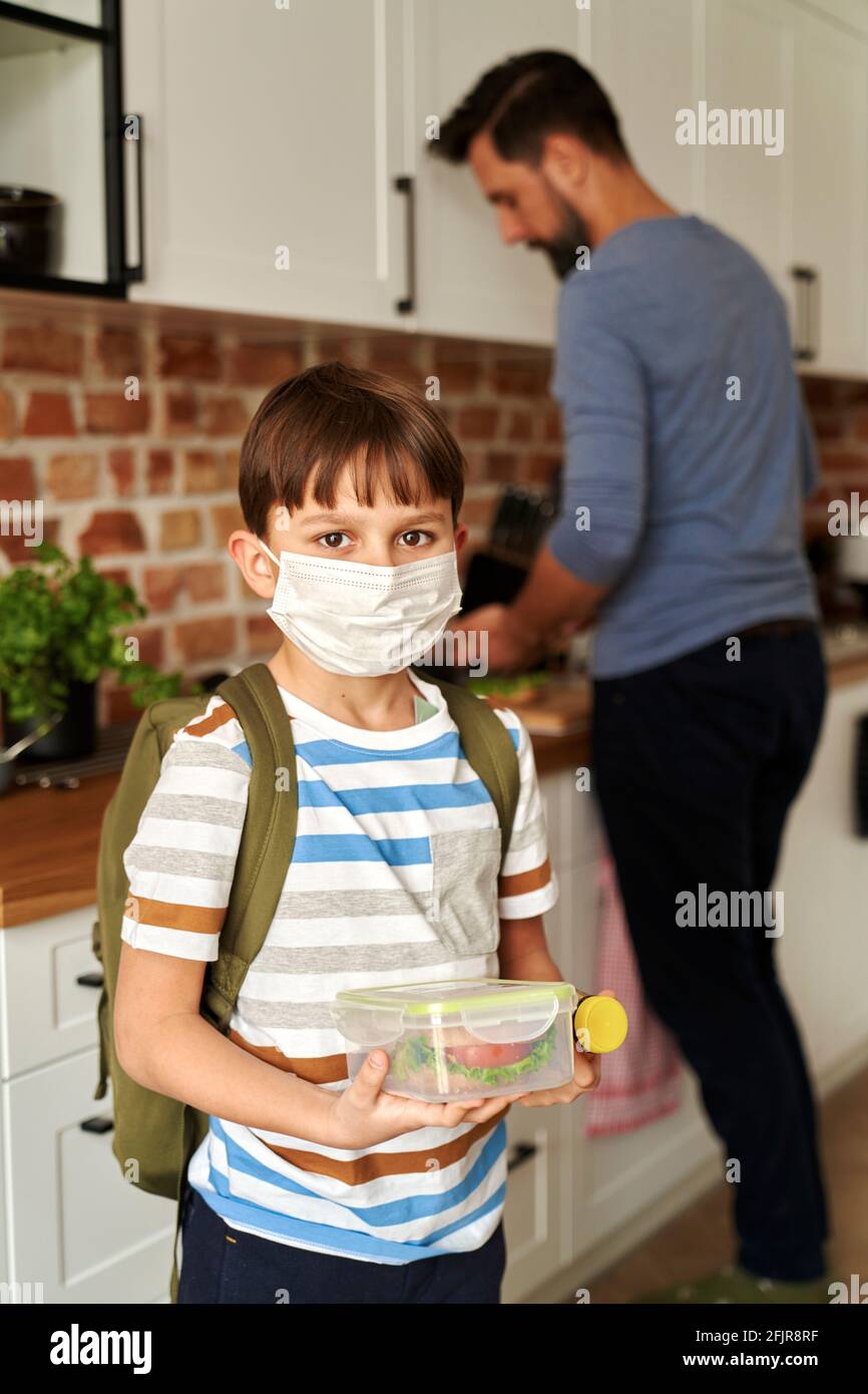 Retrato del niño en máscara protectora que sostiene la caja del almuerzo Foto de stock