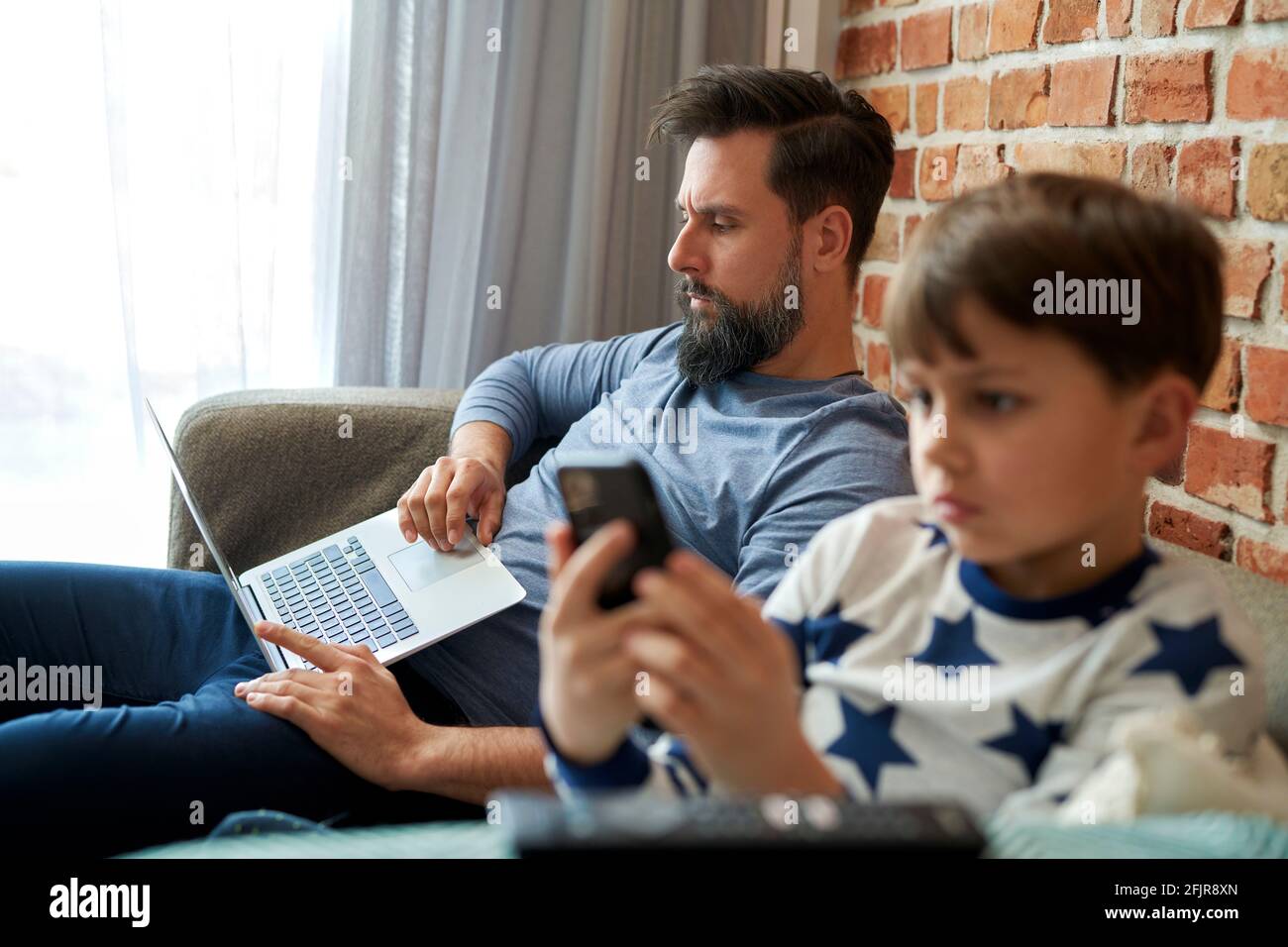 Padre trabajando en el ordenador portátil y su hijo usando el teléfono móvil Foto de stock