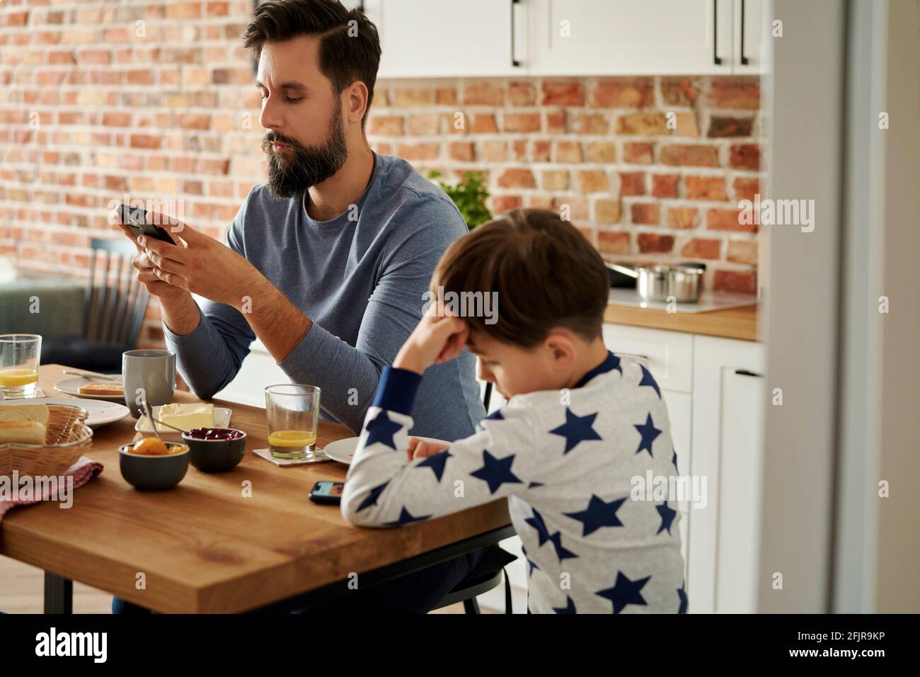 Padre e hijo usando el teléfono móvil durante el desayuno Foto de stock