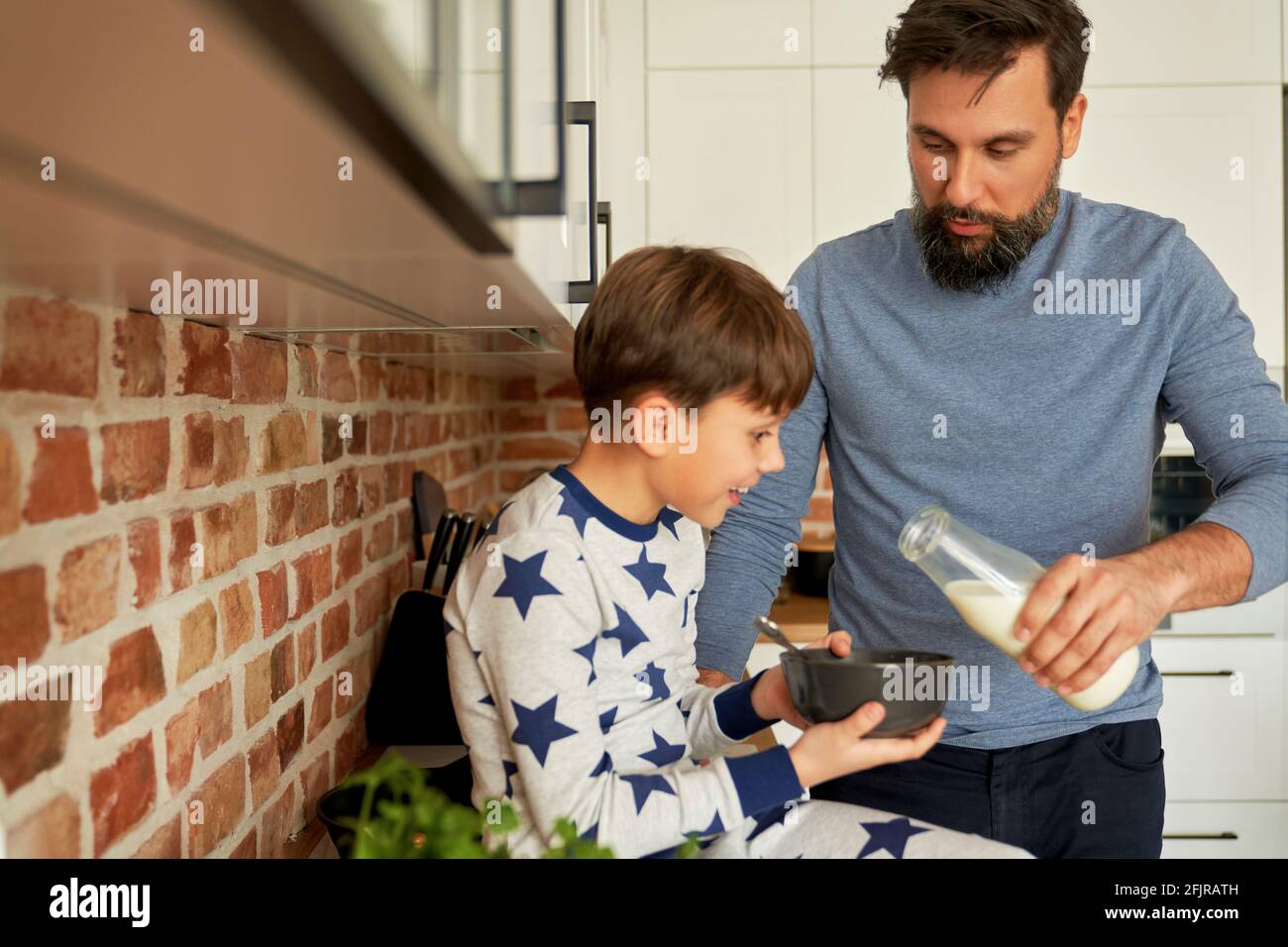 El padre vierte leche en cereal de desayuno para su hijo Foto de stock