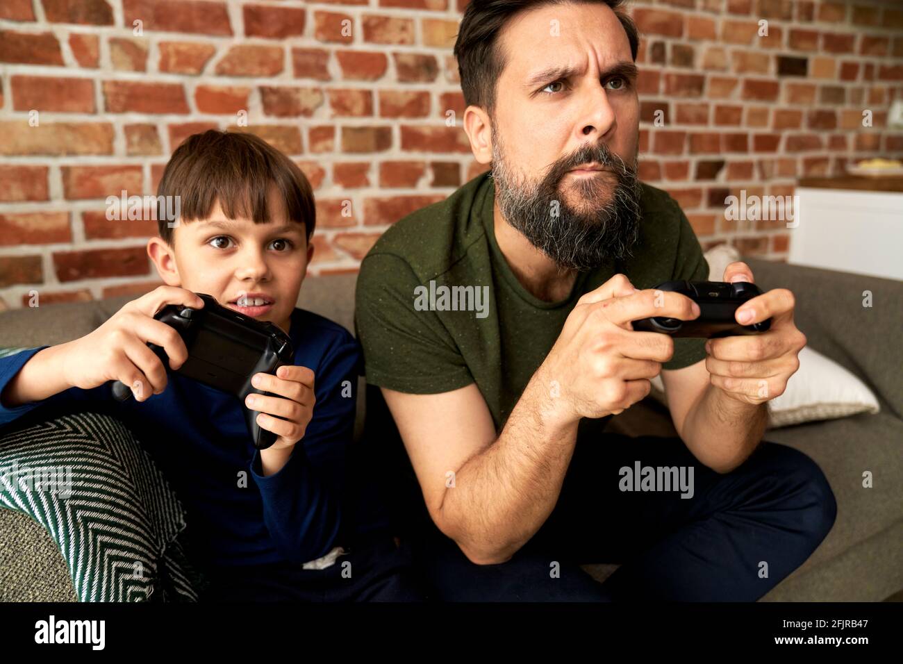 Padre y hijo enfocados sentados y jugando a videojuegos juntos Foto de stock
