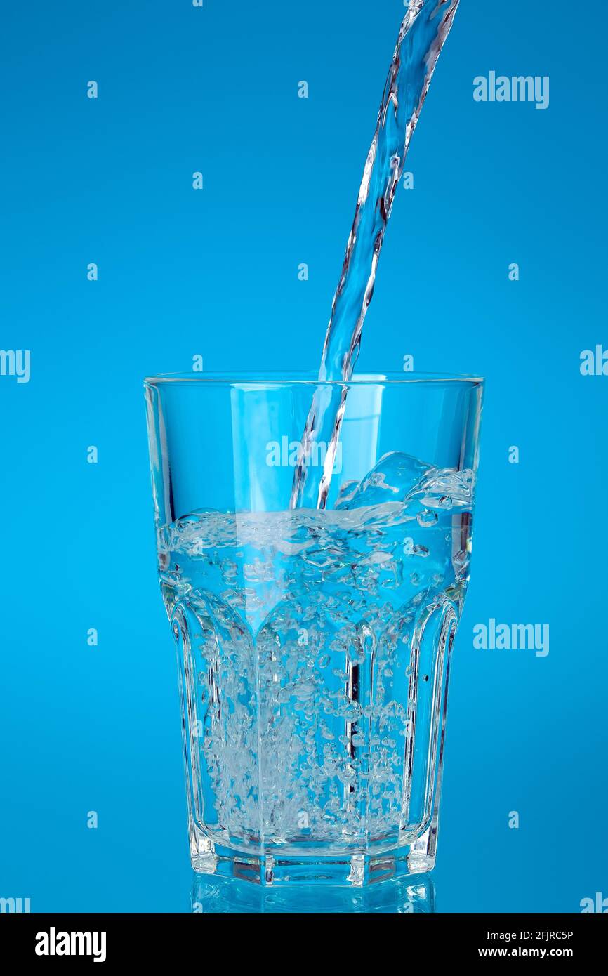 vaso de cristal lleno de una corriente de agua potable fresca con burbujas  y salpicaduras, cristalería para bebidas glasful sobre un fondo azul con un  gradiente f Fotografía de stock - Alamy