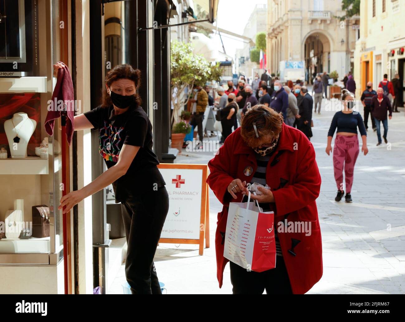 Una mujer que lleva una máscara protectora comprueba su cambio de compras  al lado de un asistente de tienda limpiando la fachada como tiendas y  servicios no esenciales reabren para el negocio