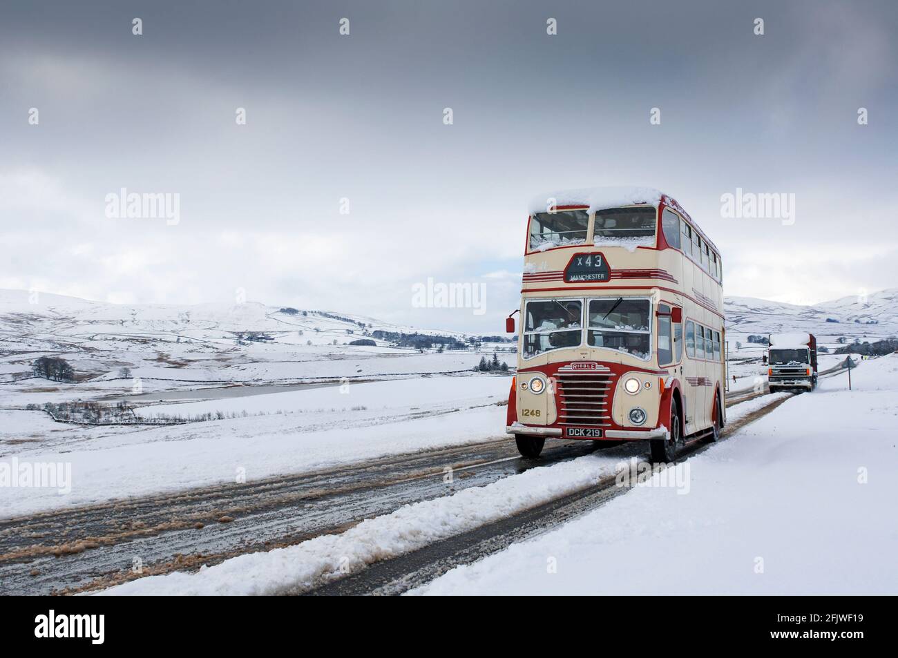 Clásico autobús de dos pisos Ribble que conduce a lo largo de una carretera nevada en Cumbria cerca de Ravenstonedale en el A684, Reino Unido. Foto de stock