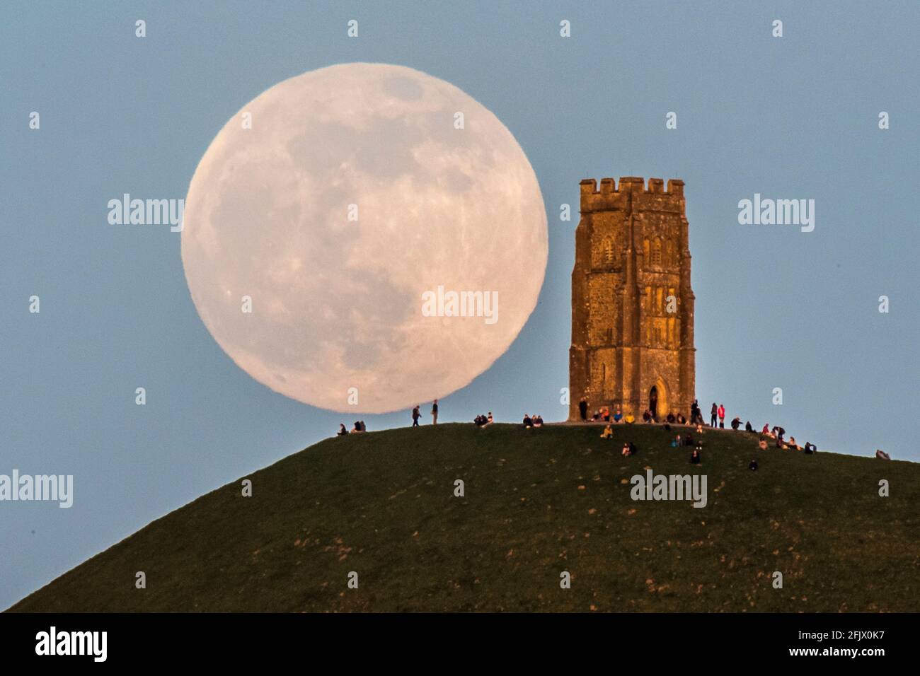 Glastonbury, Somerset, Reino Unido. 26th de abril de 2021. Clima del Reino Unido. La súper luna rosa llena se levanta desde detrás de Glastonbury Tor en Somerset en una noche clara mientras la gente se sienta en la parte superior y la mira subir. Crédito de la foto: Graham Hunt/Alamy Live News Foto de stock