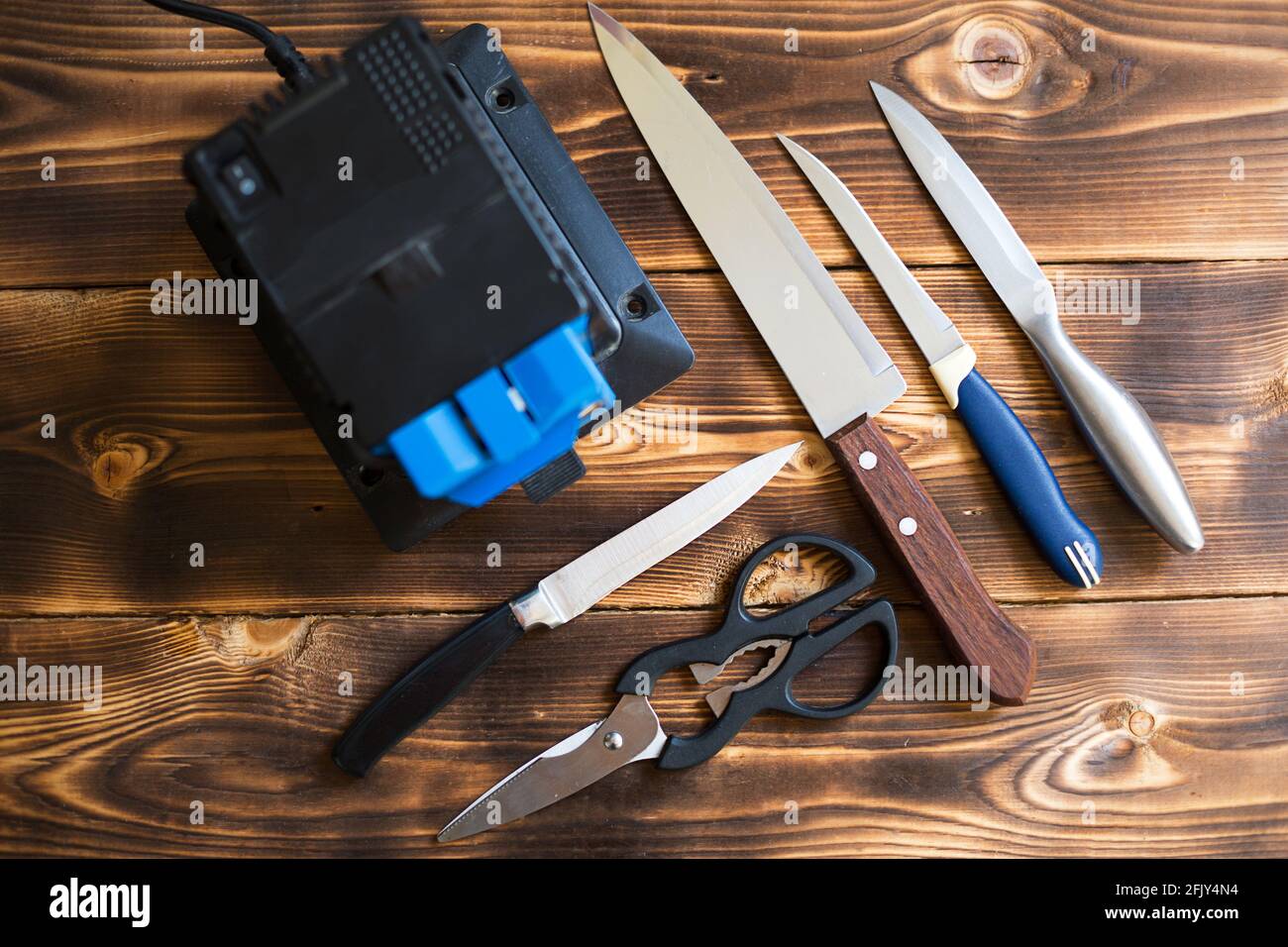 Afilar un cuchillo en un afilador eléctrico en casa. Disposición de las  cuchillas y tijeras con una máquina de afilar sobre una mesa de madera.  Vista superior, diseño plano Fotografía de stock -