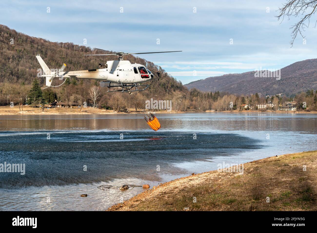 El helicóptero carga agua desde el lago Ghirla para extinguir las llamas de la montaña en Valganna, Italia. La lucha contra los incendios forestales. Foto de stock