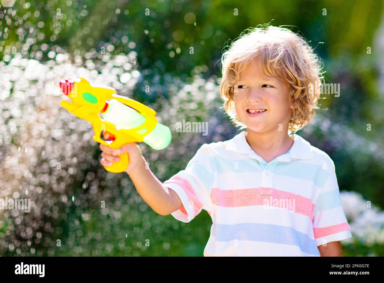 Los niños juegan con un juguete de pistola de agua en el jardín. Diversión  al aire libre en verano. Niño pequeño jugando con manguera de agua en el  soleado patio trasero. Juego