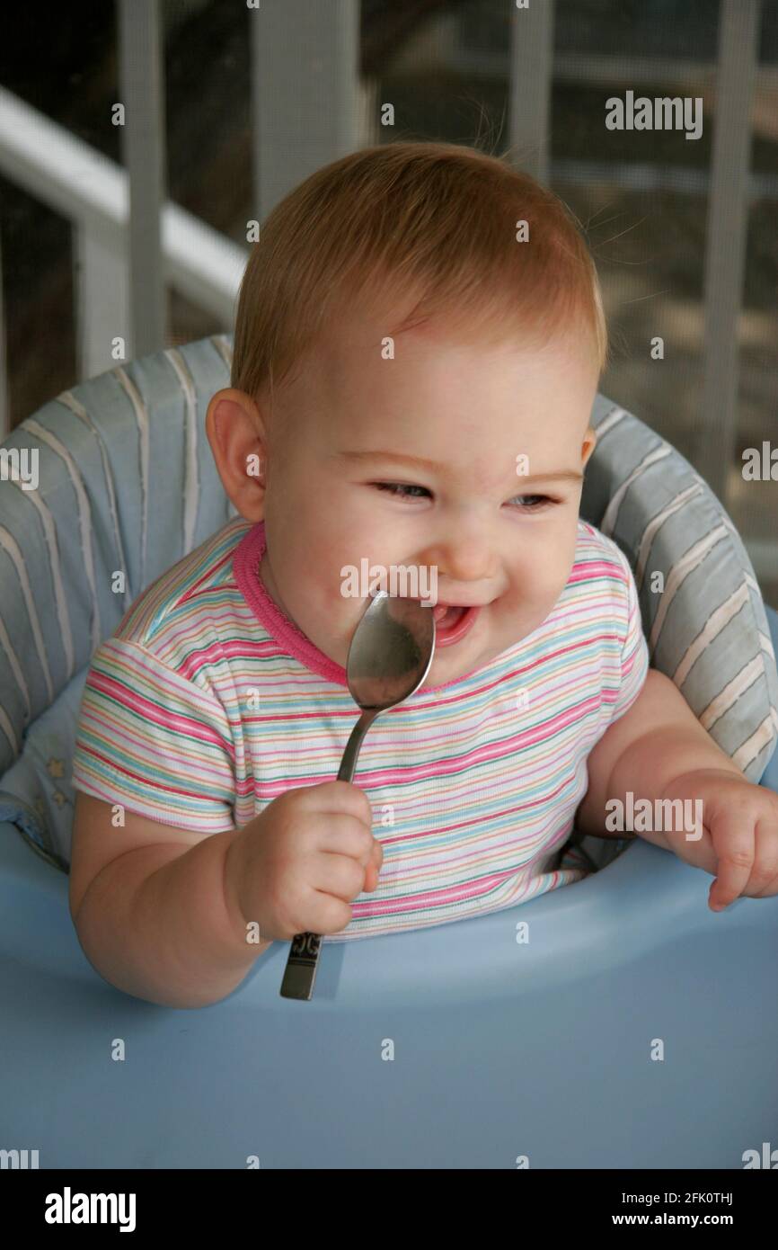 Feliz y sonriente niña de 8 meses lamer su cuchara. Foto de stock