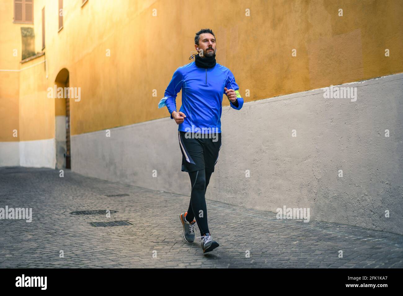 Hombre corriendo y escuchando música durante el entrenamiento. El hombre corre en la ciudad y jogging solo. Corredor con teléfono móvil conectado a una grabación de reloj inteligente Foto de stock