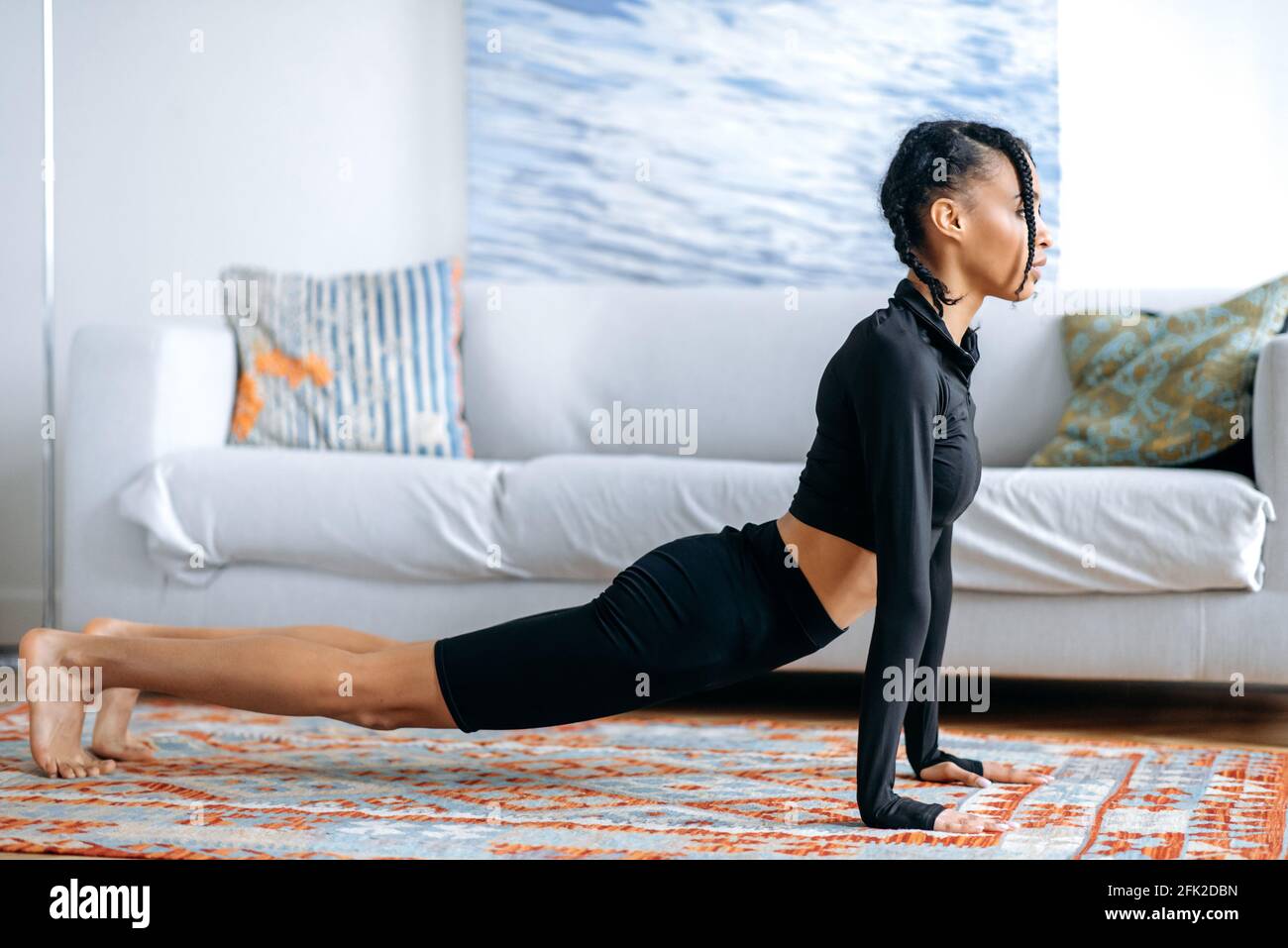 Atractiva chica americana africana delgada activa en ropa deportiva negra,  estirando en casa en el suelo, se dedica a la aptitud, lleva un estilo de  vida saludable, el cuidado de la salud