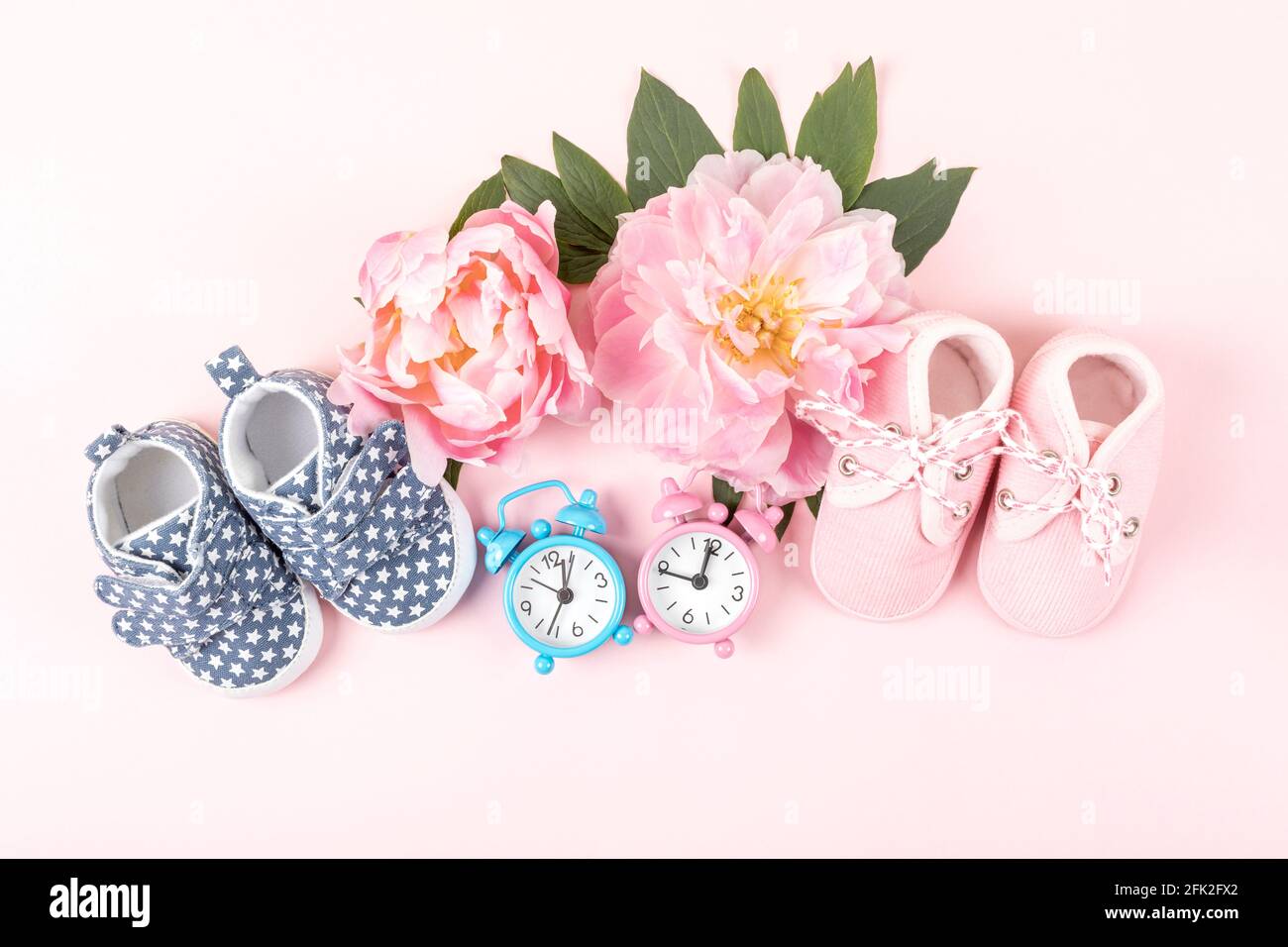 Zapatos de niña y niño con relojes de color rosa y azul sobre fondo rosa.  Cumpleaños del bebé, invitación o tarjeta de felicitación mockup. Espacio  de copia. Capa plana Fotografía de stock -