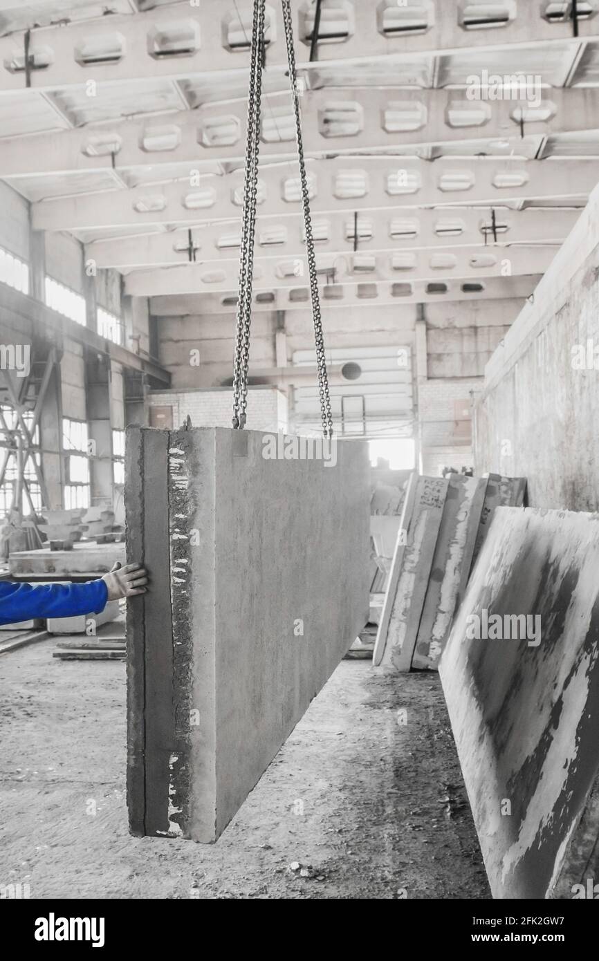La mano de un trabajador de la construcción sostiene una gran placa de  hormigón en un elevador con una cadena en una producción de barras de una  empresa industrial Fotografía de stock -