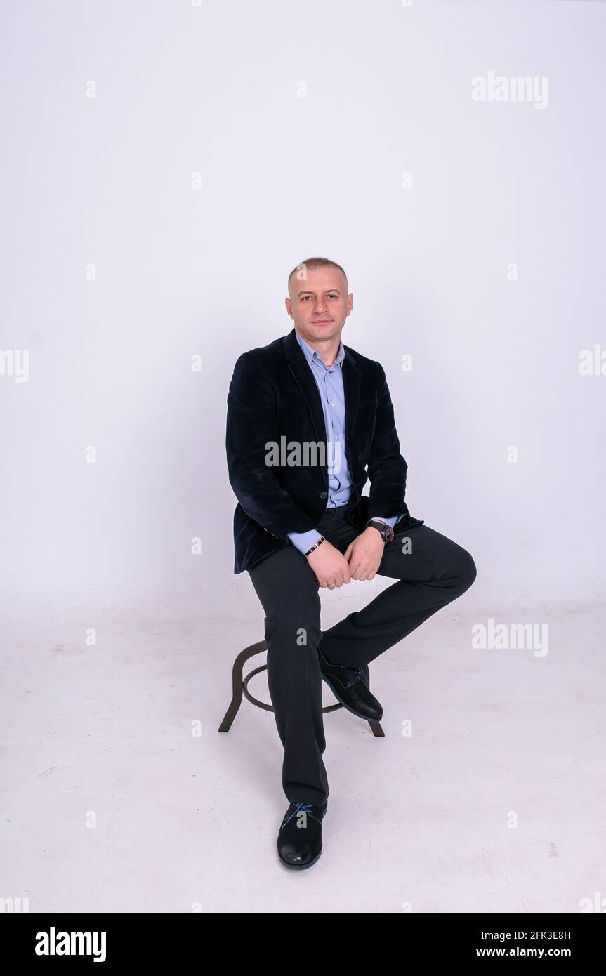 Un hombre con una camisa azul, un pantalón negro y una azul se sienta sobre un taburete sobre un fondo blanco Fotografía de stock - Alamy
